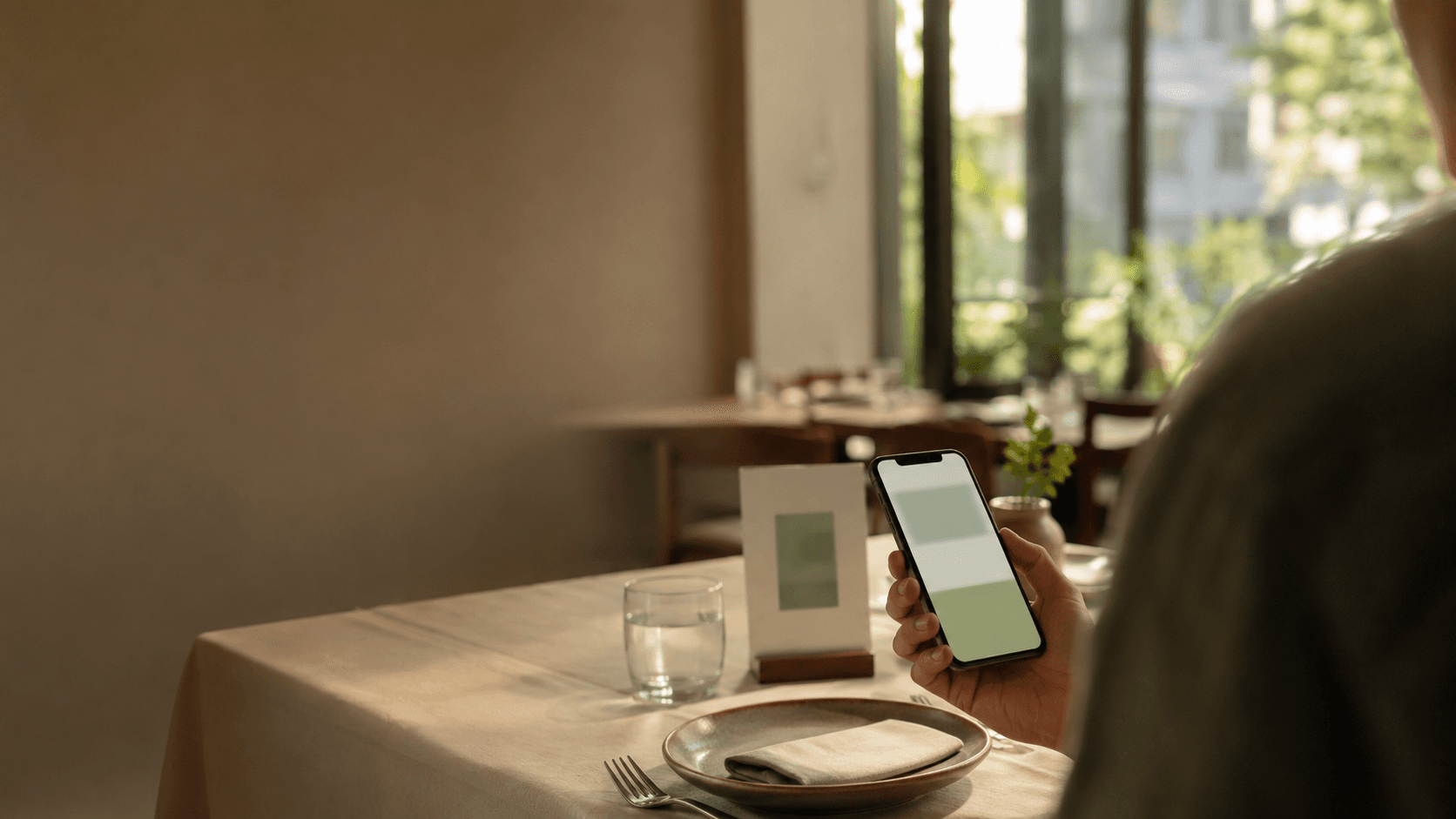 A guest holding a phone at a dine-in table, with a QR stand beside the place setting